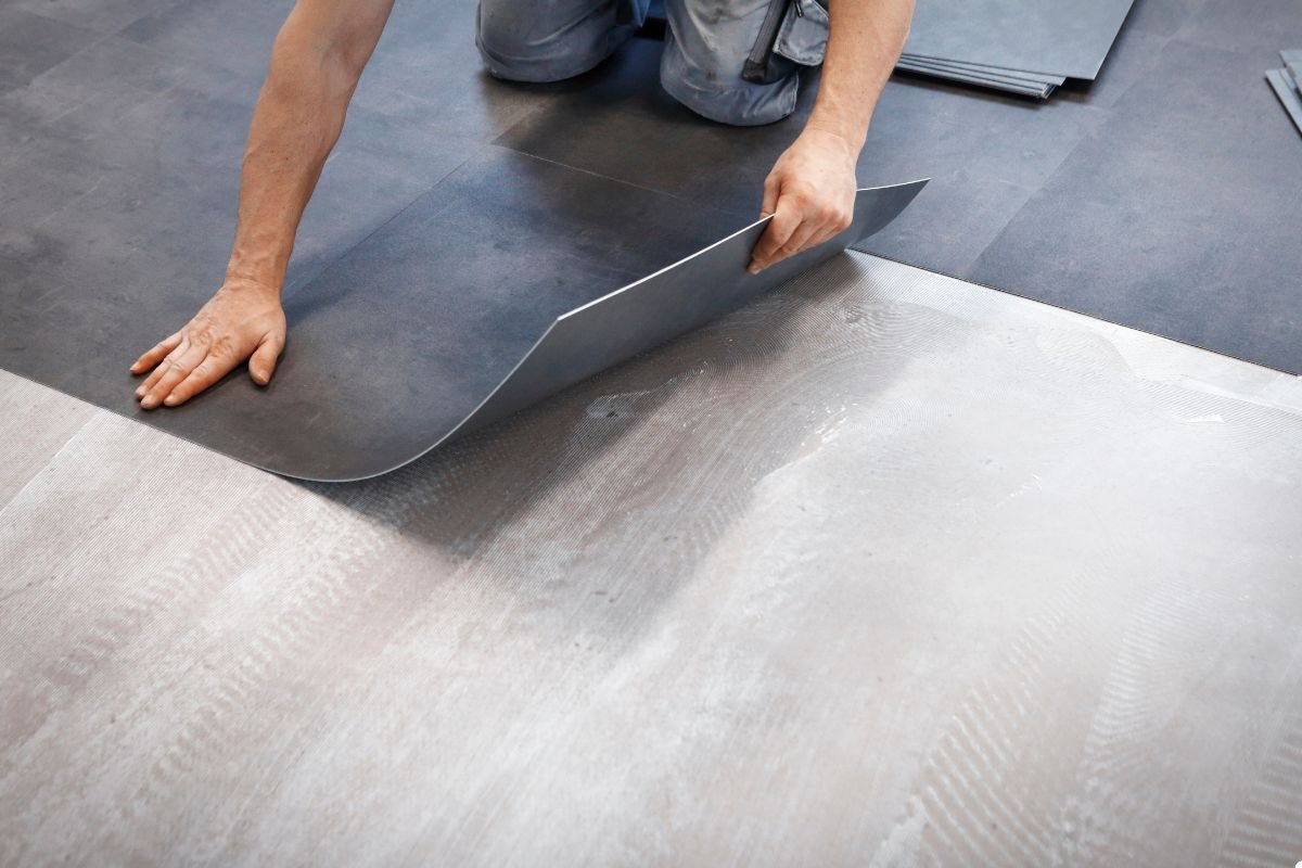 A man carefully lays down a piece of vinyl flooring on a smooth surface, ensuring a precise fit.