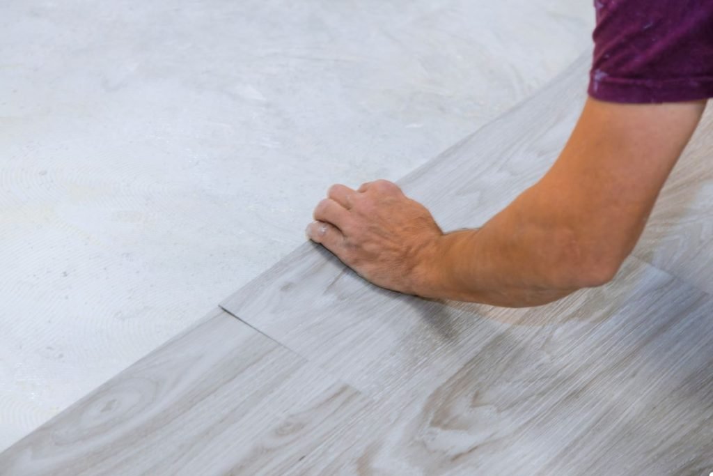 A man is installing laminate flooring, focused on aligning the planks in a bright, spacious area.