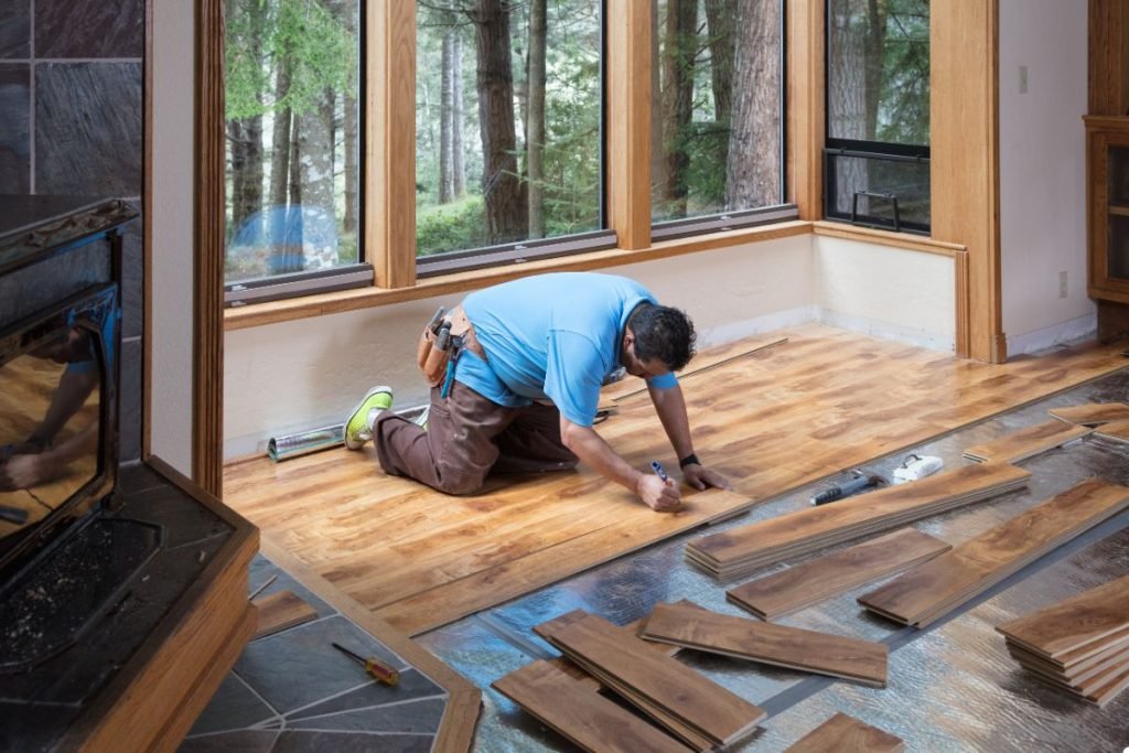 A man is focused on installing a wooden floor in a well-lit room, showcasing craftsmanship and attention to detail.
